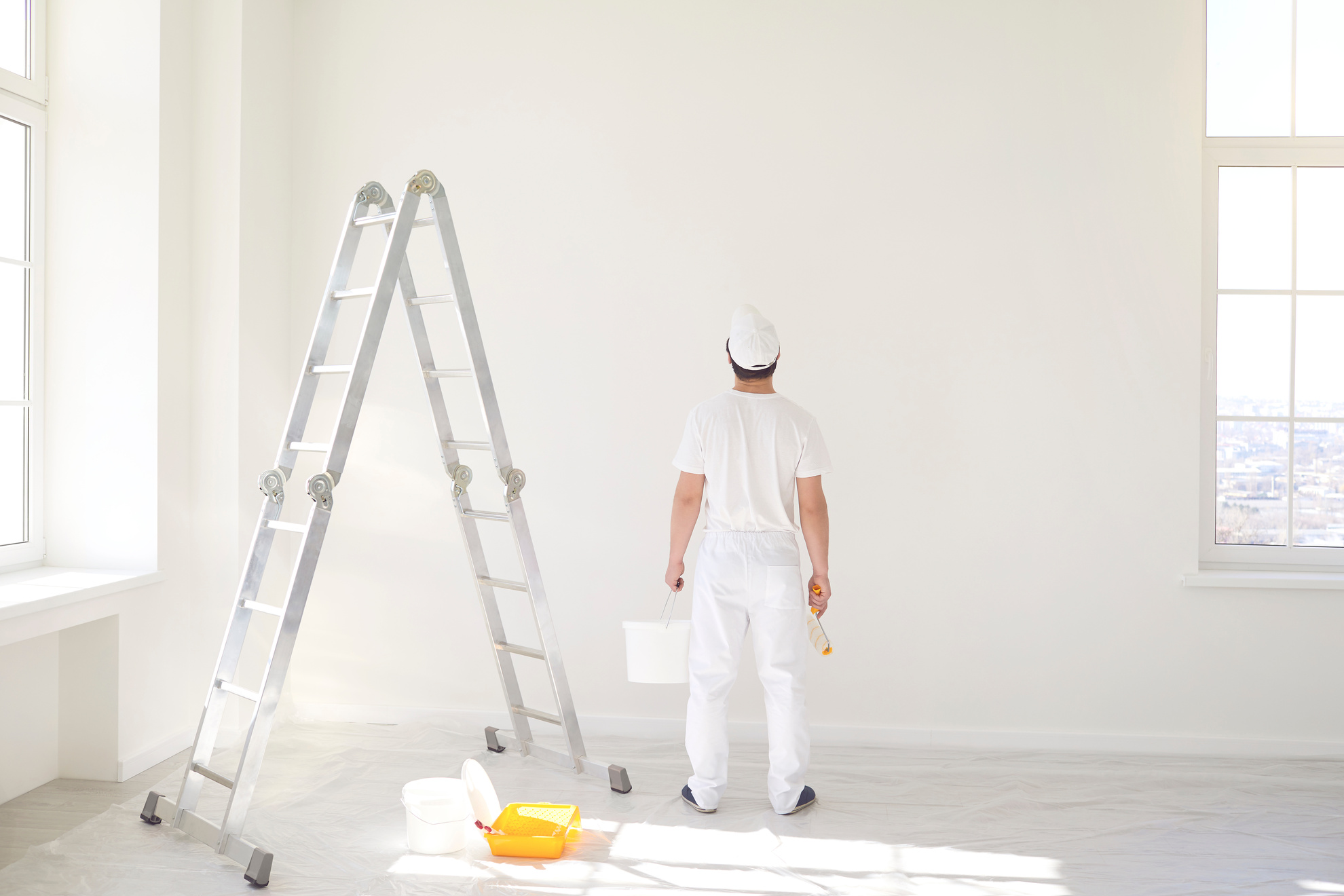 A Male Painter in a White Uniform with a Roller Works in His Hand in a White Room